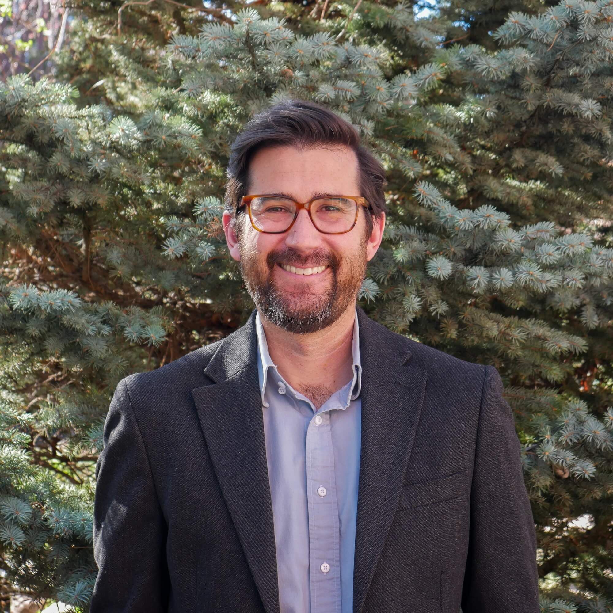 Aaron Citron Headshot in front of a large evergreen