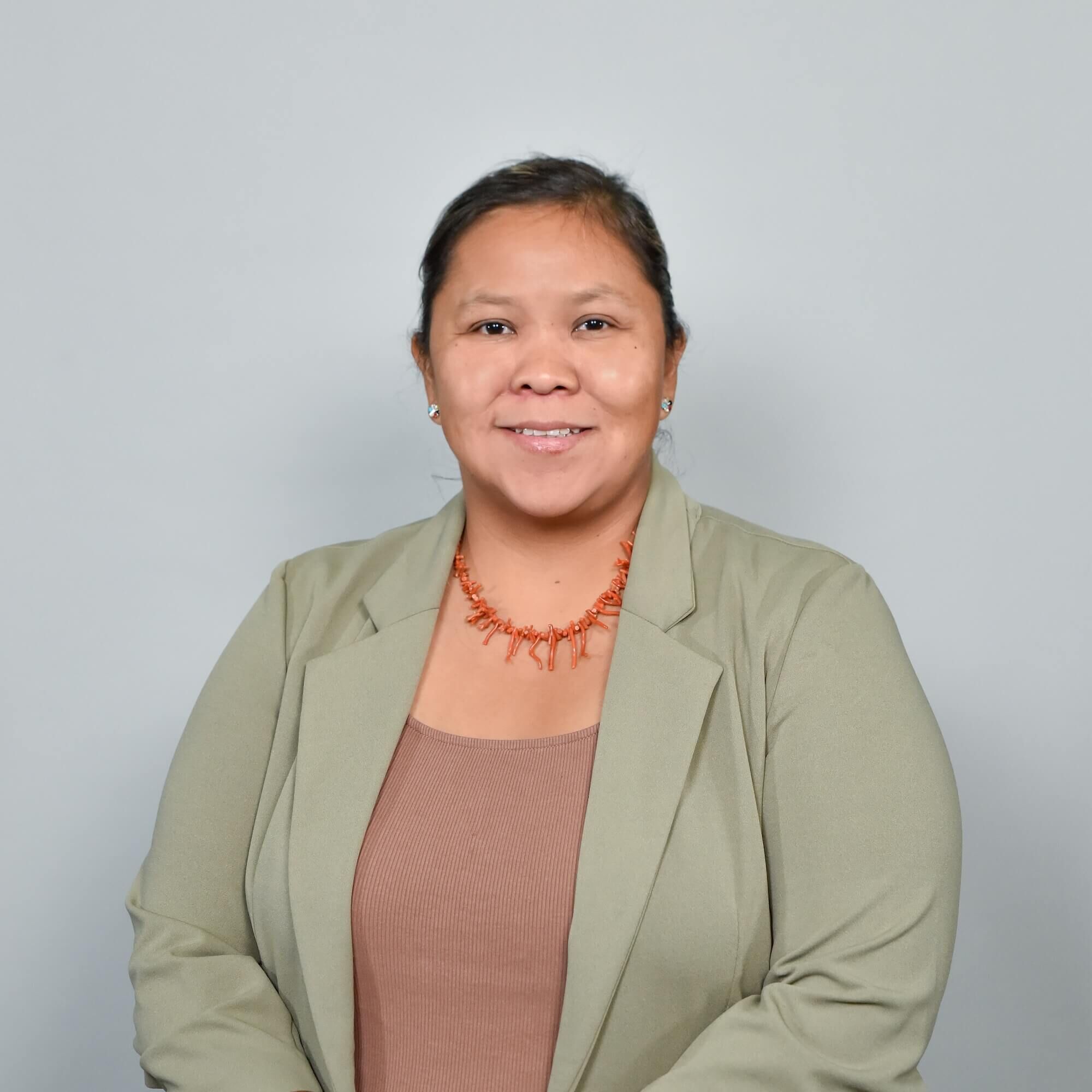 Letisha Yazzie headshot in a green jacket with an orange necklace against a grey backdrop